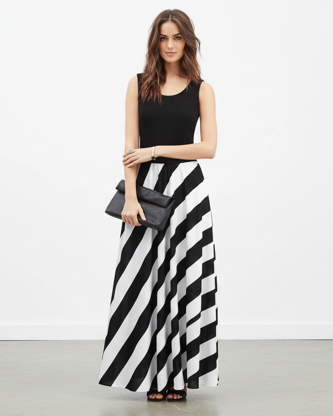 Woman wearing a black sleeveless top and black and white striped skirt with a gray clutch.