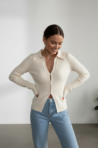 Woman wearing a cream ribbed cardigan and light blue jeans against a plain background