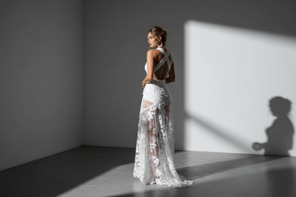 Woman in a white lace wedding dress standing in a sunlit room with a soft shadow on the wall.
