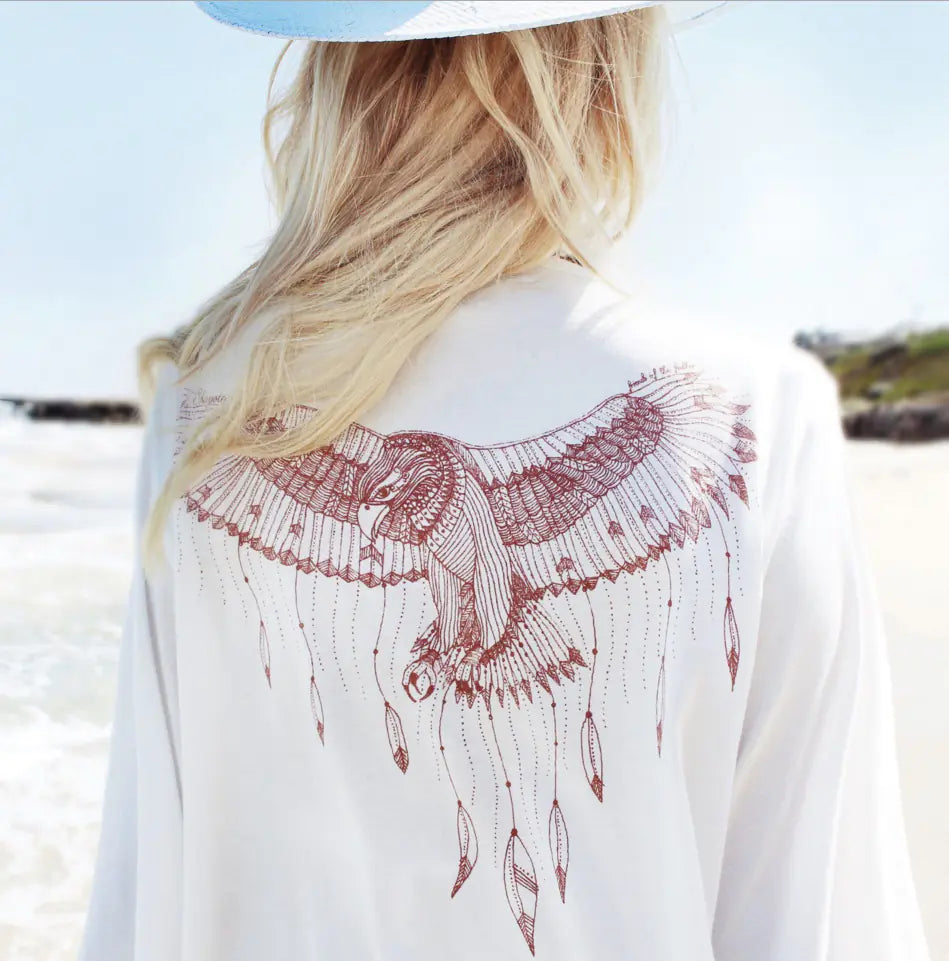 Person wearing a white shirt with a red owl design on a beach.