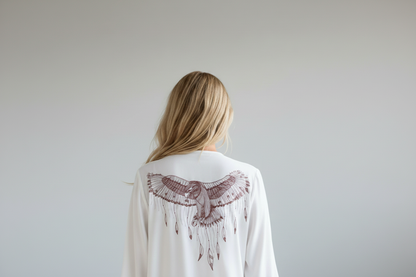 Woman wearing a white cardigan with a bird design on the back against a plain background