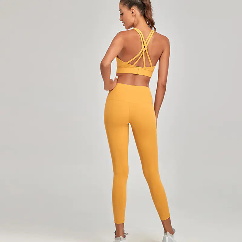 Woman wearing a yellow sports bra and leggings set on a gray background