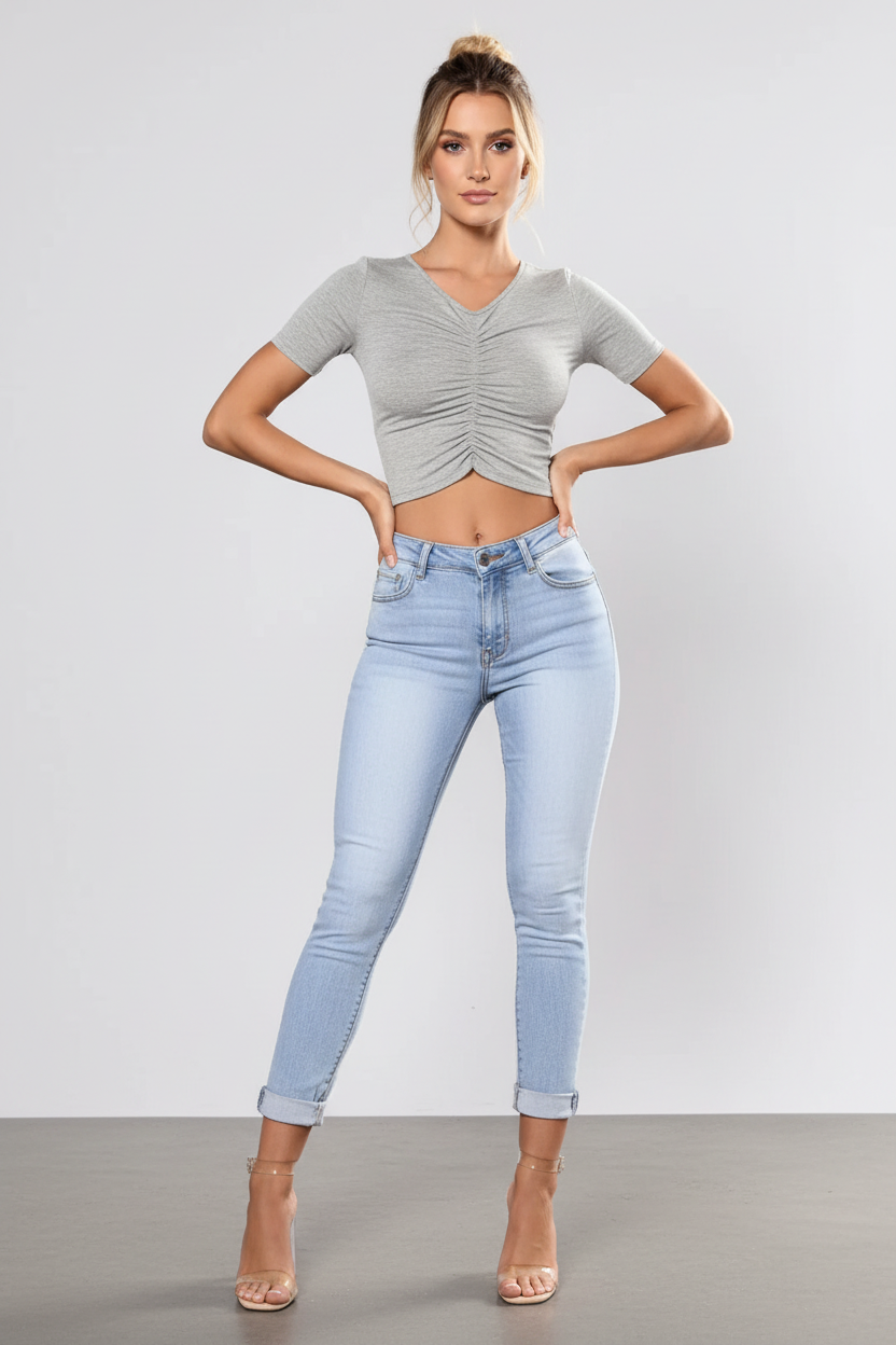 Woman wearing a gray ruched top and light blue jeans against a plain background