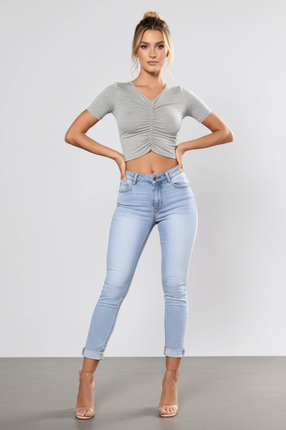 Woman wearing a gray ruched top and light blue jeans against a plain background