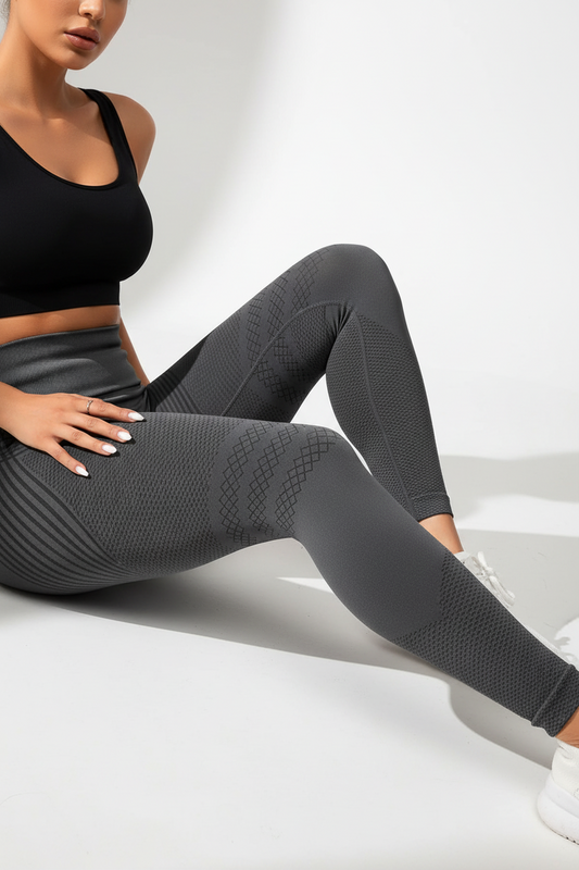 Person wearing black sports bra and gray leggings sitting on a white surface.