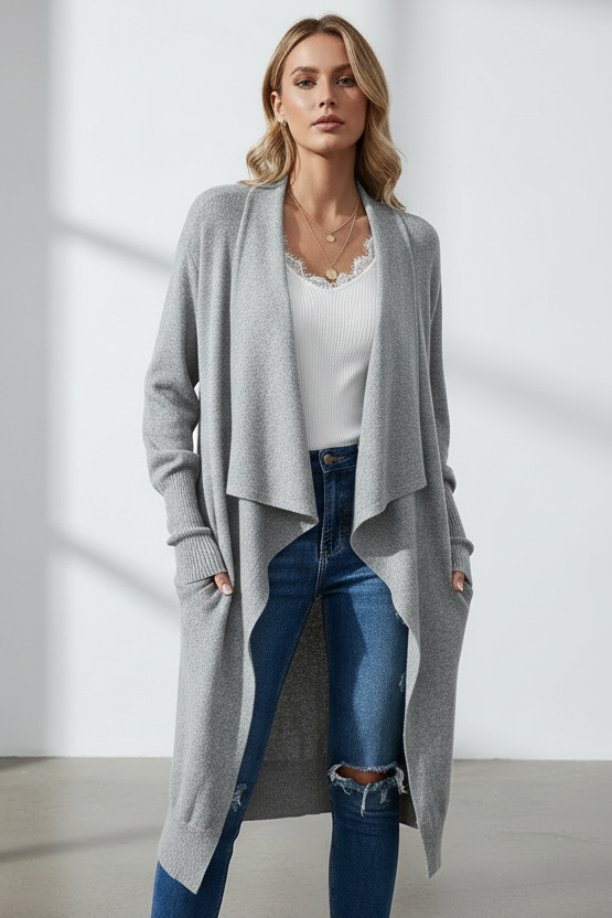 Woman wearing a long gray cardigan over a white top and blue jeans in a minimalistic setting.