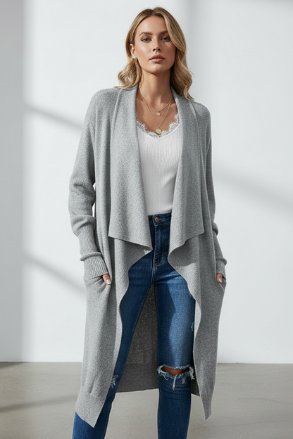 Woman wearing a long gray cardigan over a white top and blue jeans in a minimalistic setting.