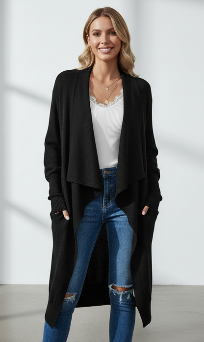 Woman wearing a black long cardigan over a white top and blue jeans on a plain background