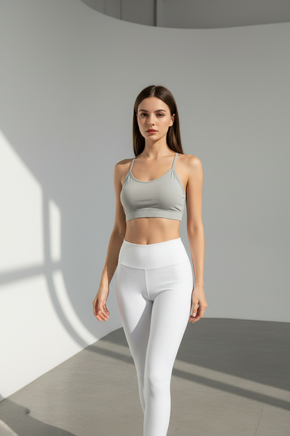 Woman wearing a gray sports bra and white leggings in a minimalistic setting
