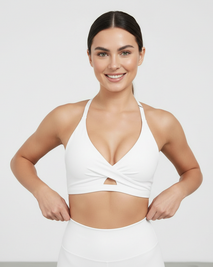 Woman wearing a white sports bra and leggings on a plain background