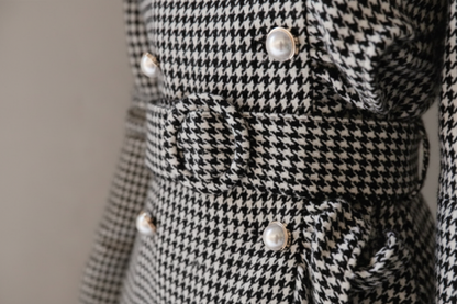 Close-up of a houndstooth patterned coat with pearl buttons on a neutral background